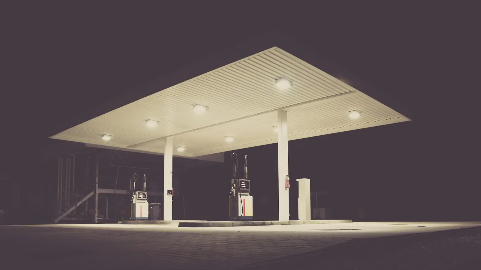 Self-serve gas station lit up under a large white canopy at night, with two pump islands